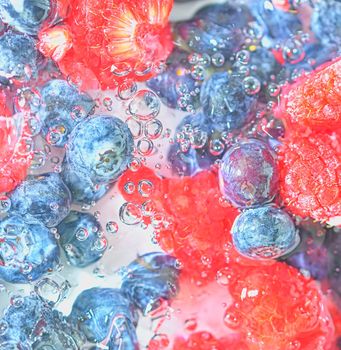 Water with fresh berries, close-up. Close-up view of the blueberries and raspberries in water background. Texture of bilberries and raspberries with macro bubbles on the glass wall. Flat design, top view. Horizontal image. Defocused.