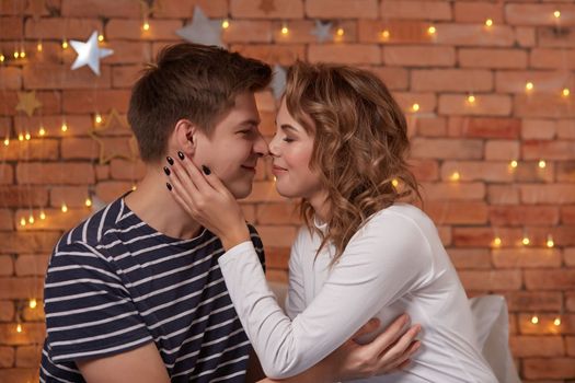 Happy loving couple relaxing on bed at home, young man touching smiling beautiful woman face, looking in the eyes enjoying togetherness and tenderness in love, close up view