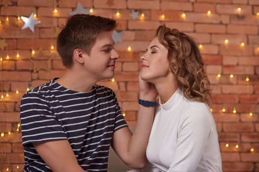 Happy loving couple relaxing on bed at home, young man touching smiling beautiful woman face, looking in the eyes enjoying togetherness and tenderness in love, close up view