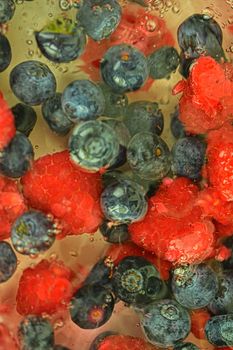 Water with fresh berries, close-up. Close-up view of the blueberries and raspberries in water background. Texture of bilberries and raspberries with macro bubbles on the glass wall. Flat design, top view. Vertical image. Defocused.