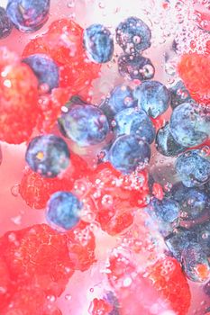 Water with fresh berries, close-up. Close-up view of the blueberries and raspberries in water background. Texture of bilberries and raspberries with macro bubbles on the glass wall. Flat design, top view. Vertical image. Defocused.