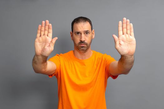 Bearded hispanic man wearing casual orange t-shirt turning away hands showing rejection and denial with scared and disgusting expression. Stop and prohibited.