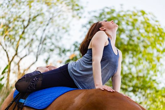 young woman doing yoga on a horse against the backdrop of trees.