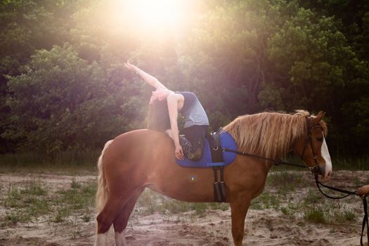 young woman doing yoga on a horse against the backdrop of trees.