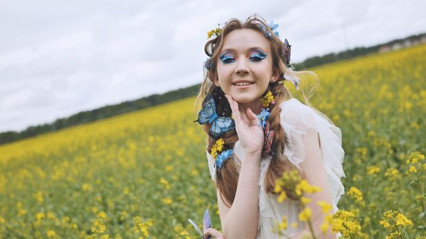 A young girl poses in a rapeseed field with a beautiful hairdo of flowers and butterflies