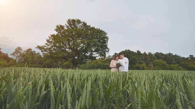 A young couple with their newborn baby in green wheat in a field