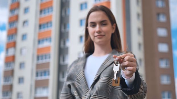 The girl shows the keys to the apartment against the backdrop of an apartment building