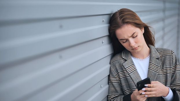 A disgruntled girl stares into a smartphone against a striped wall