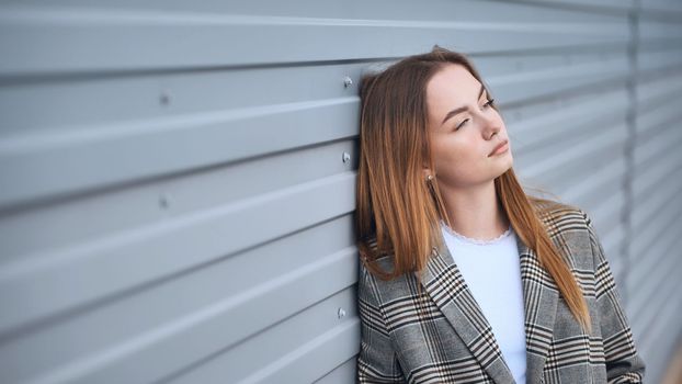 A pensive, sad girl at the striped wall of the house