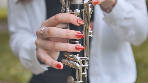 A girl plays the clarinet in the summer in the park. Close-up of her hands