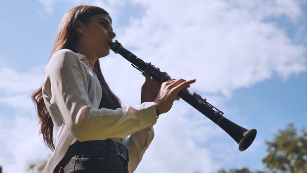 Girl plays clarinet against sky