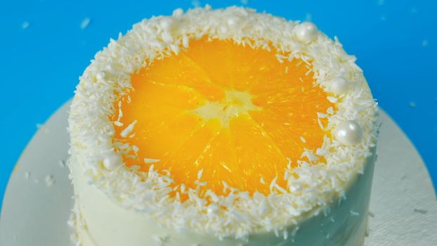Cake with orange and coconut shavings spinning on a blue background