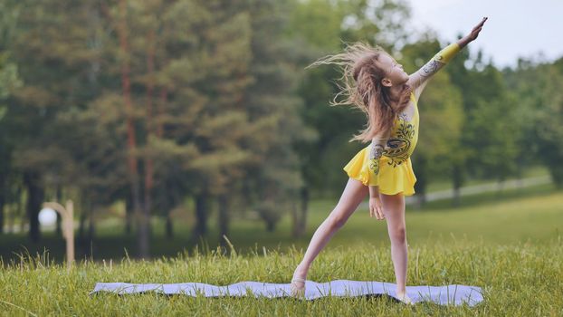 A little girl performs the elements of rhythmic gymnastics in the park