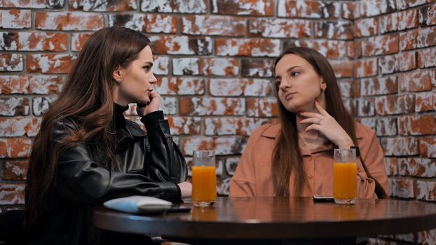 Two brown-haired girls talk in a cafe over glasses of juice