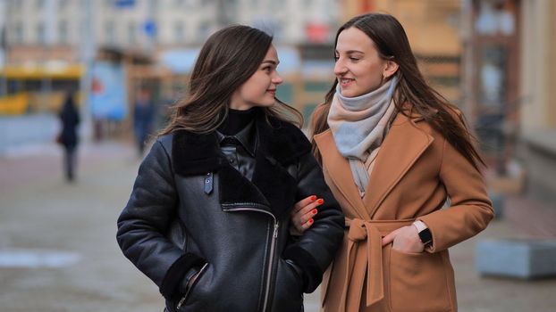 A friend comes up from behind her waiting girlfriend on a city street