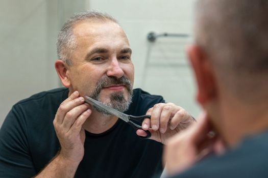 Portrait of Middle-aged handsome man cutting his beard with scissors