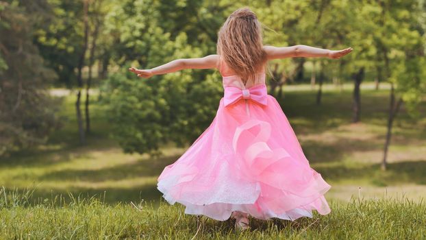 A girl in a pink princess dress is spinning in the park