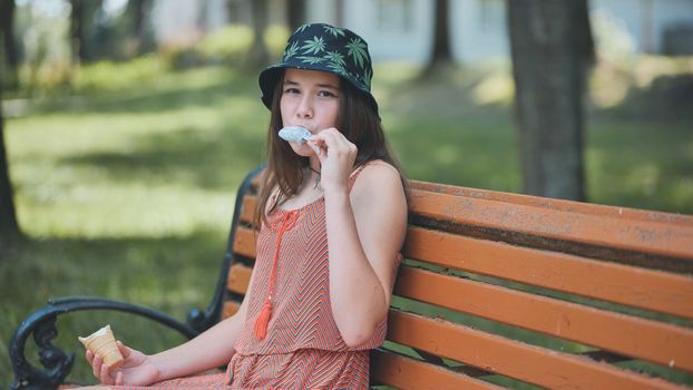 Teenage girl eating ice cream in the park on the bench