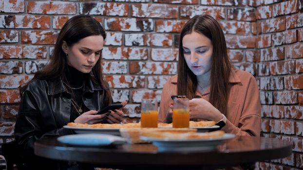 Two beautiful girls are sitting in a cafe and talking with phones