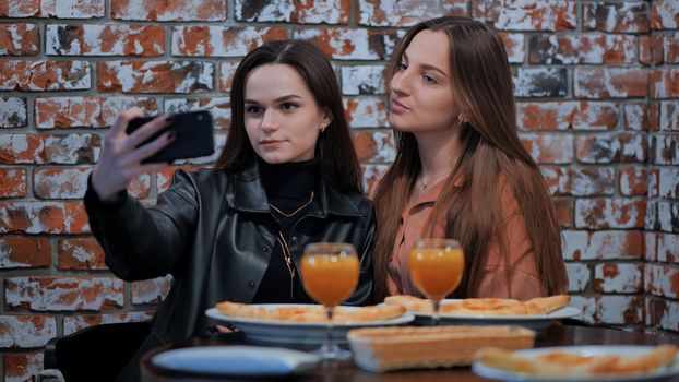 Two girls are sitting in a cafe and taking a selfie on the phone