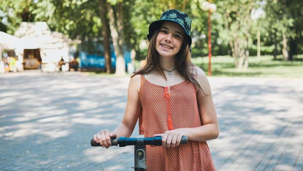 Portrait of a girl on an electric scooter posing in a park in the summer