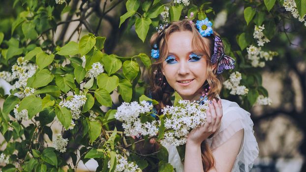 A young girl poses in white lilac with a beautiful hairstyle of flowers and butterflies