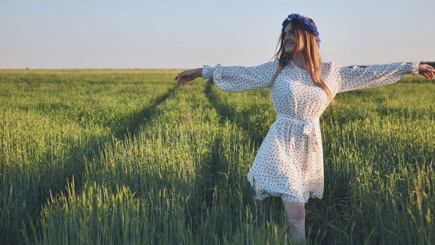 A young Ukrainian girl walks through a young wheat field