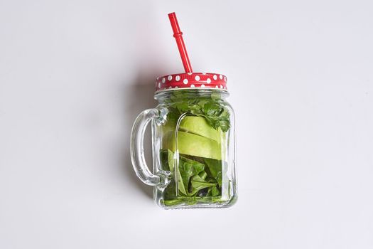an apple in a glass jar with a straw and a red straw sticking to it's side on a white surface
