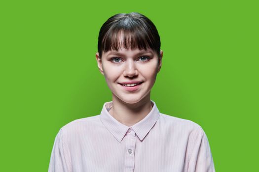 Headshot portrait of young smiling female looking at camera on green color studio background. Happy pretty teenage girl 18, 19 years old. Lifestyle, beauty, emotion, face, youth concept