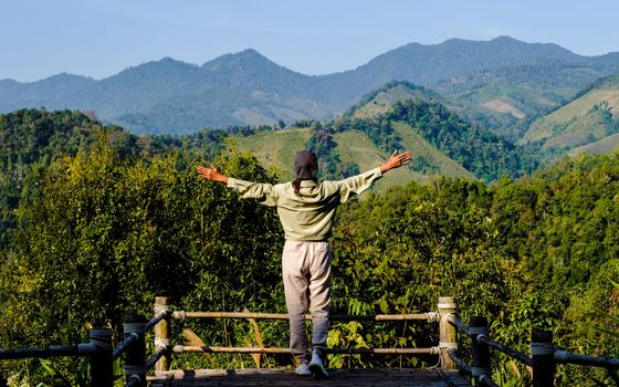 Asian women with hands up looking out over the mountains of Northern Thailand Nan Sapan valley.