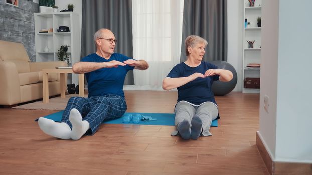 Cheerful senior couple training together sitting on yoga mat. Old person healthy and active lifestyle exercise and workout at home, elderly training and fitness