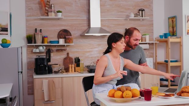 Couple doing online shopping on laptop during breakfast. Entering information, customer using e-commerce technology buying stuff on the web, cosumerism banking and ordering