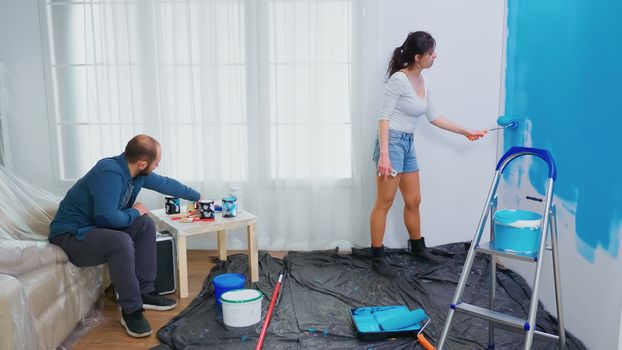 Wife painting wall with roller brush during home decorating. Couple in home decoration and renovation in cozy apartment flat, repair and makeover