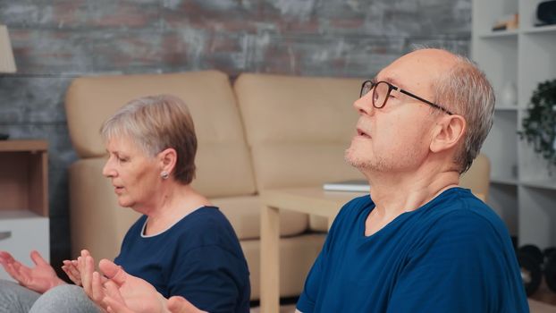 Active senior couple meditating together in living room. Old person healthy and active lifestyle exercise and workout at home, elderly training and fitness
