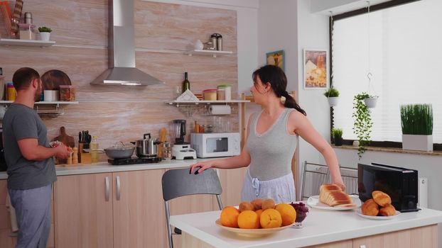 Smiling wife using electric toaster to make roasted bread for breakfast. Housewife using electric toaster to make roasted bread, addition to a delicious breakfast for her and her husband