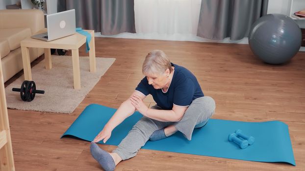 Active senior woman stretching body on yoga mat. Old person pensioner exercise training at home sport activity at elderly retirement age