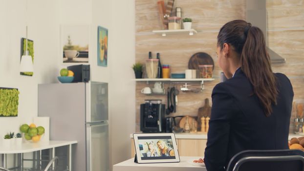 Business woman during a video call with sister while eating breakfast. Using modern online internet web technology to chat via webcam videoconference app with relatives, family, friends and coworkers