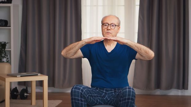 Elderly man exercising in living room sitting on stability ball. Old person pensioner healthy training healthcare sport at home, exercising fitness activity at elderly age