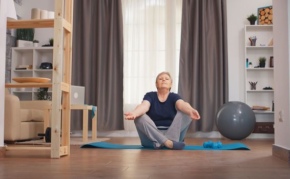Senior woman relaxing in living room doing yoga. Active healthy lifestyle sporty old person training workout home wellness and indoor exercising