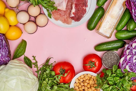 some vegetables and meat on a pink surface with an egg, lemons, tomatoes, cucumls, lete, eggs