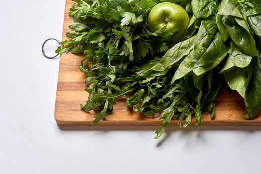 some greens on a cutting board with an apple in the top left and green leaves to the bottom right side