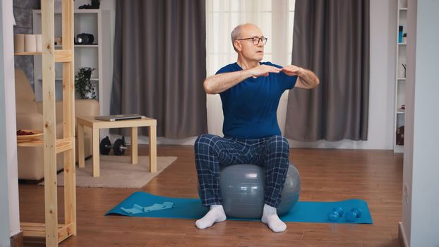 Senior man training on stability ball in living room. Old person pensioner healthy training healthcare sport at home, exercising fitness activity at elderly age