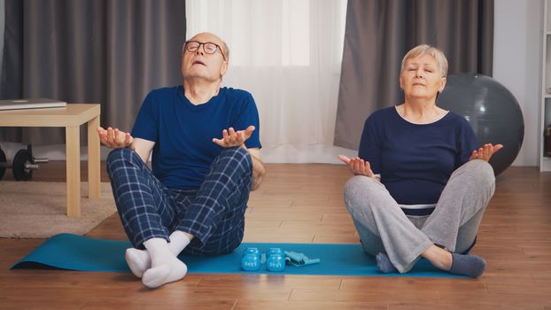 Senior couple doing breathing exercise on yoga mat in living room. Old person healthy lifestyle exercise at home, workout and training, sport activity at home