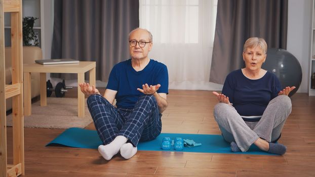 Senior couple doing yoga sitting on mat in living room. Old person healthy lifestyle exercise at home, workout and training, sport activity at home