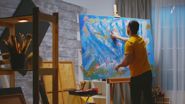Artwork with fingers using colorful oil paint on large canvas in studio.