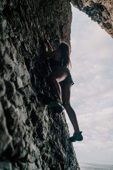 A girl climbs a rock. The athlete trains in nature. Woman overcomes difficult climbing route. Extreme hobby. Tourist woman rock climber hiking on mountains rocks over beautiful sea coast