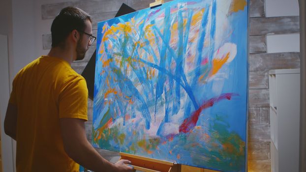Artist paints on large canvas with fingertips in art studio.