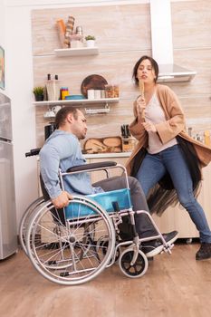 Disabled man in wheelchair singing with his wife in kitchen. Young couple having fun.