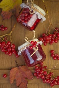 Viburnum fruit jam in a glass jar on a wooden table near the ripe red viburnum berries. Source of natural vitamins.