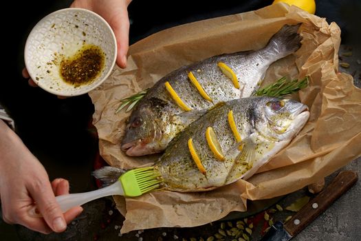 Fresh raw dorado or sea bream with lemon, herbs, olive oil and spices on black background, top view with copy space